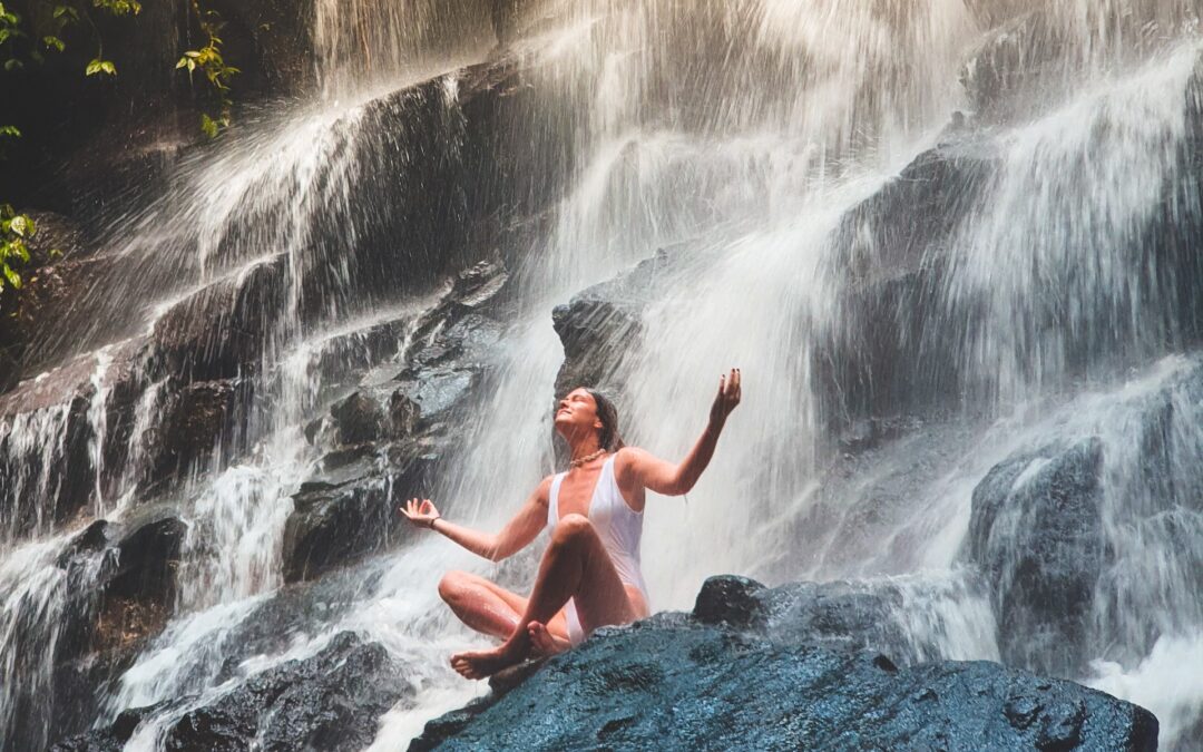 Woman meditating at bottom of waterfall.